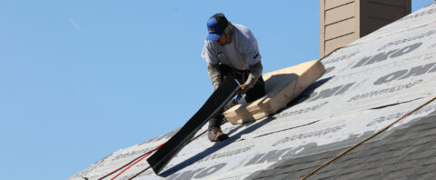 A roofer installing materials on a roof deck covered with underlayment.