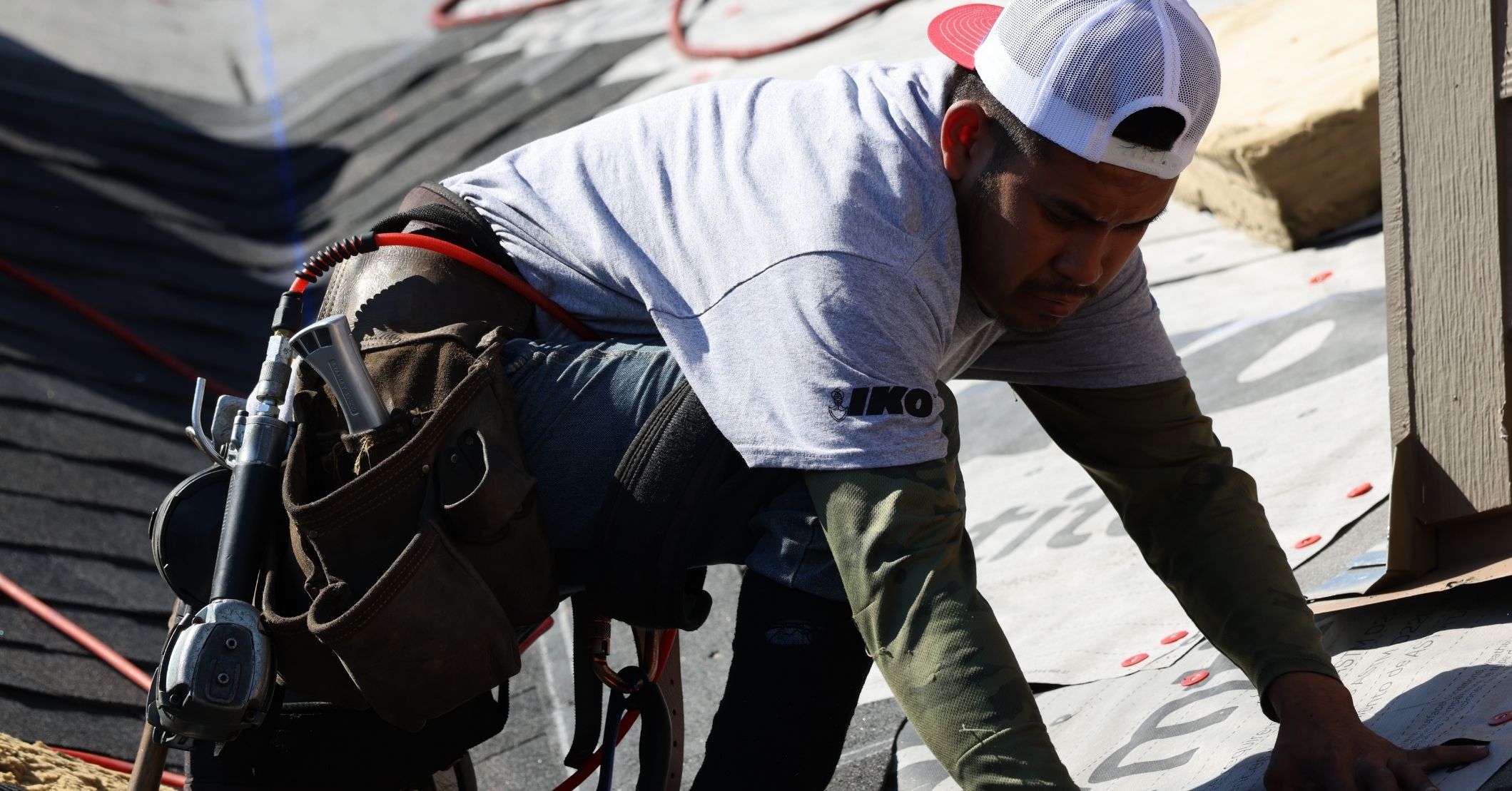 Un couvreur portant un t-shirt IKO pose des bardeaux et une sous-couche tout en portant un harnais de couvreur.