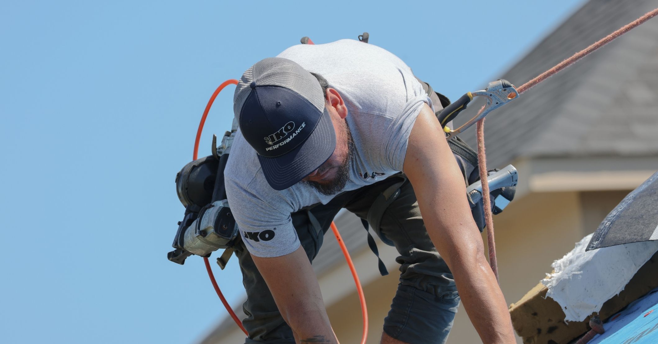 Un couvreur portant des vêtements IKO installe des bardeaux sur un toit tout en portant un harnais pour toiture.