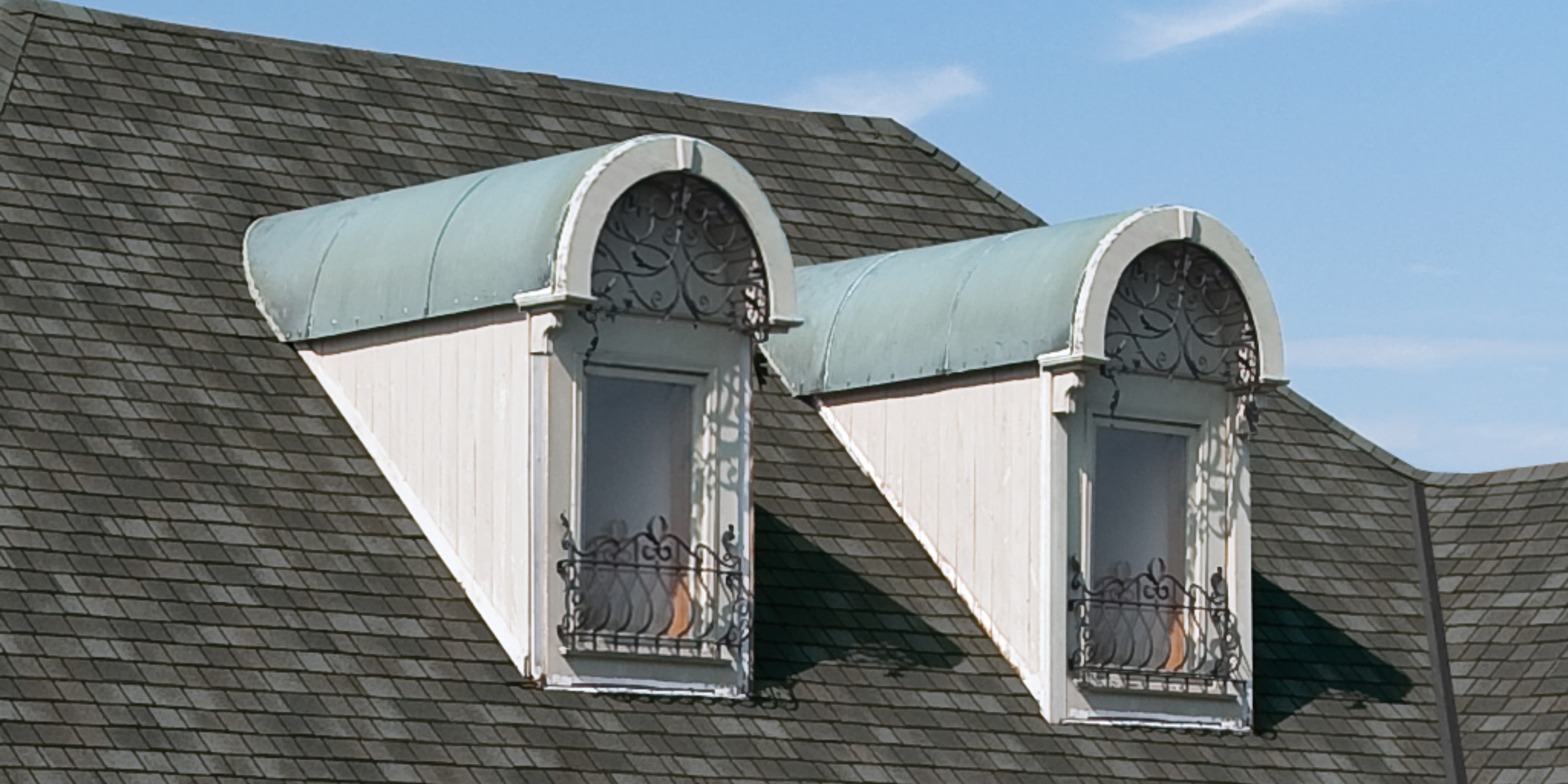 Two barrel dormers with rounded copper roofs and decorative window grilles installed on a dark grey shingle roof, representing a luxurious architectural style.