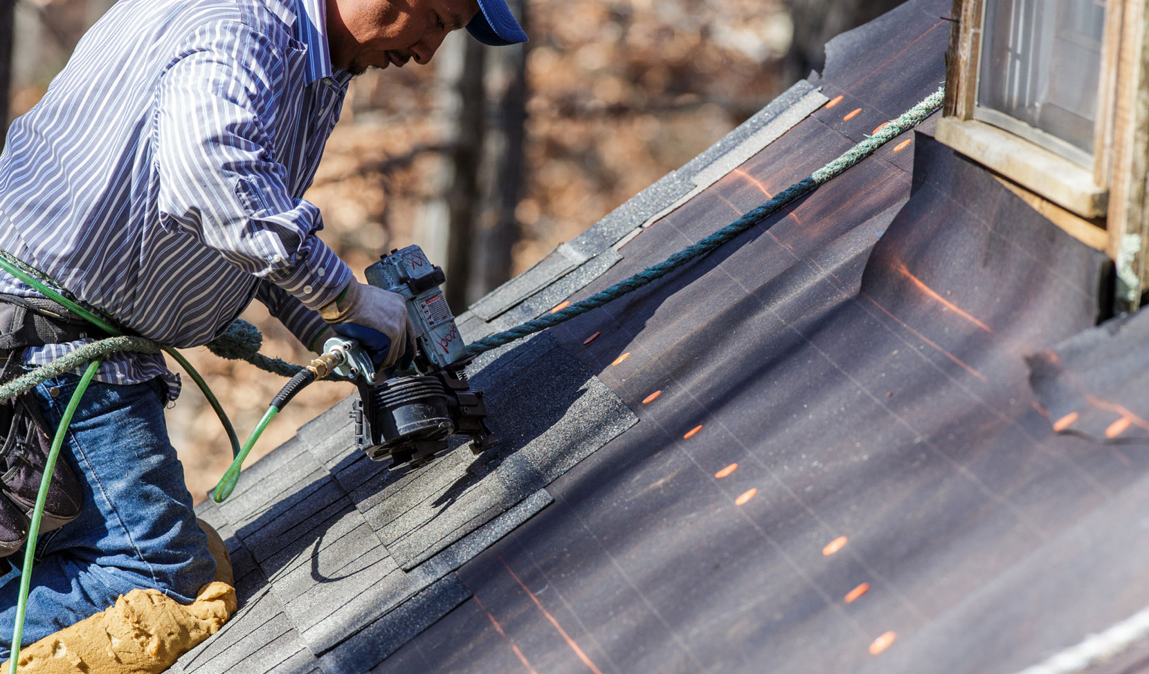 contractor using a nail gun to install shingles