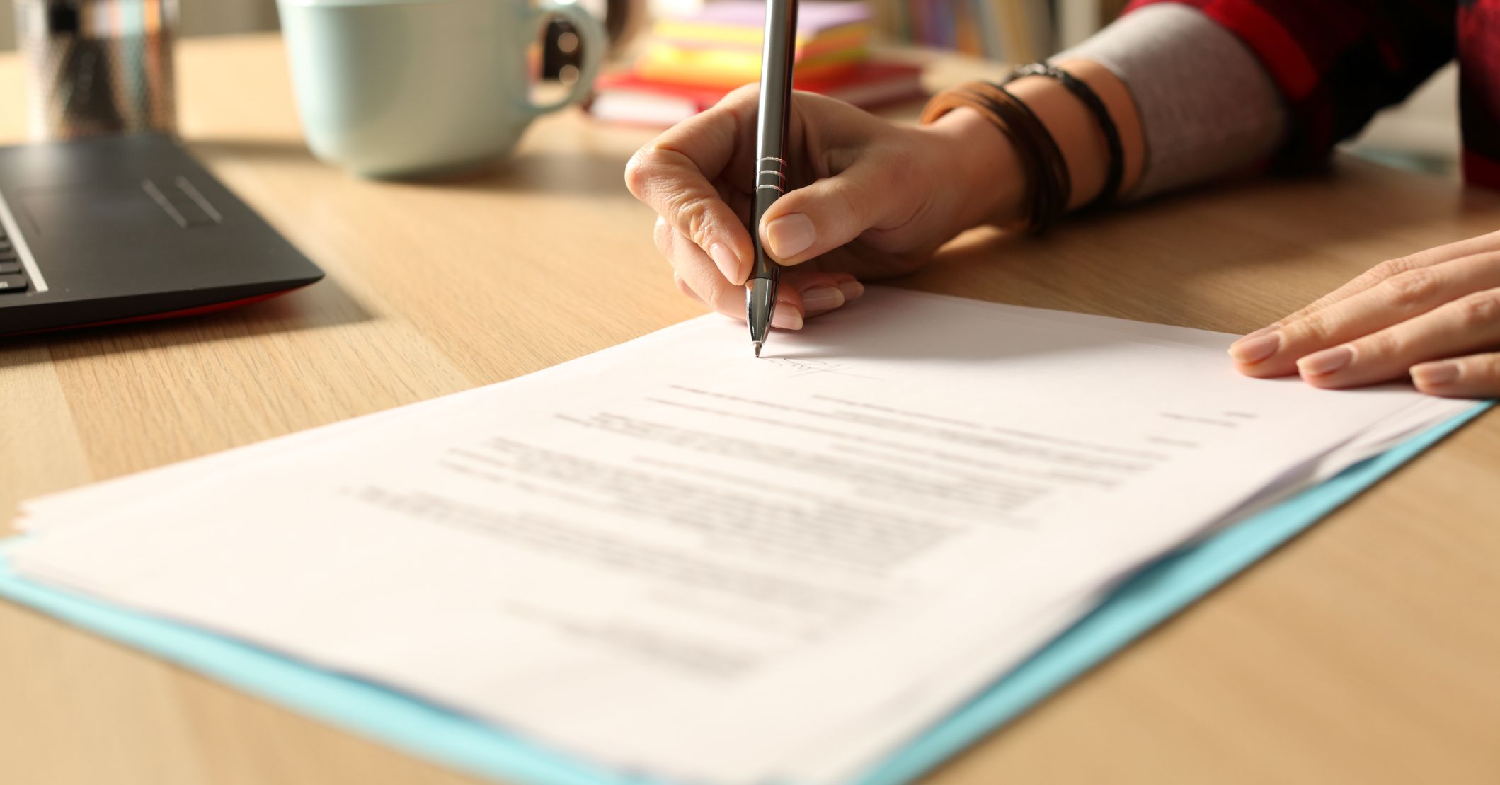 Person signing a home improvement financing contract or estimate document on a wooden desk.