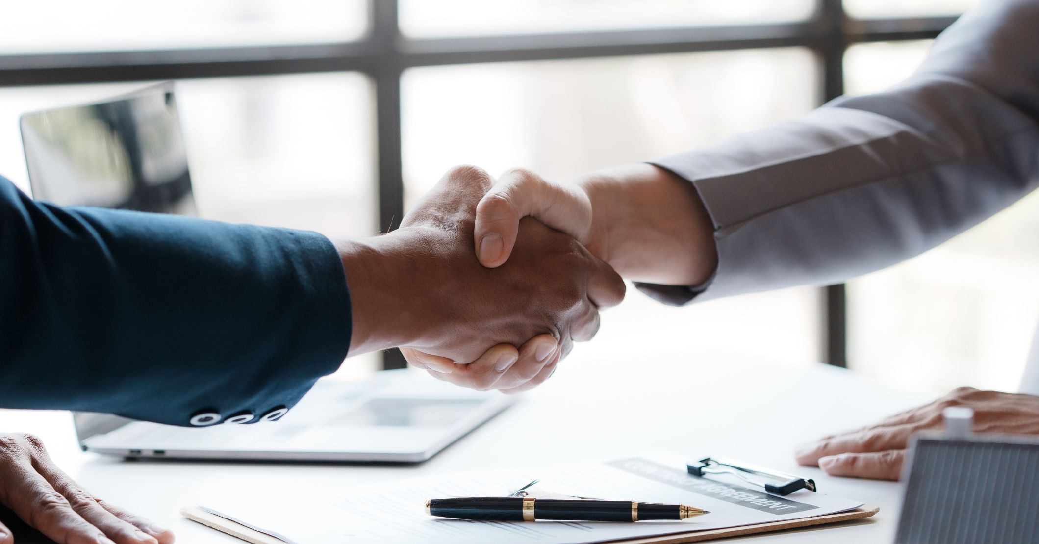Contractor and client shaking hands over a desk after finalizing a roofing project agreement.