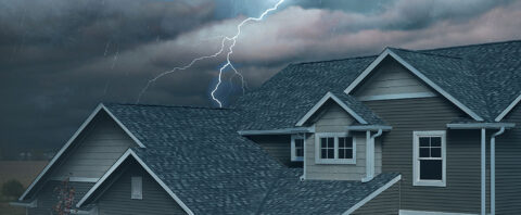 Dark storm clouds and lightning over a modern home with asphalt shingles, demonstrating weather-resistant roofing.