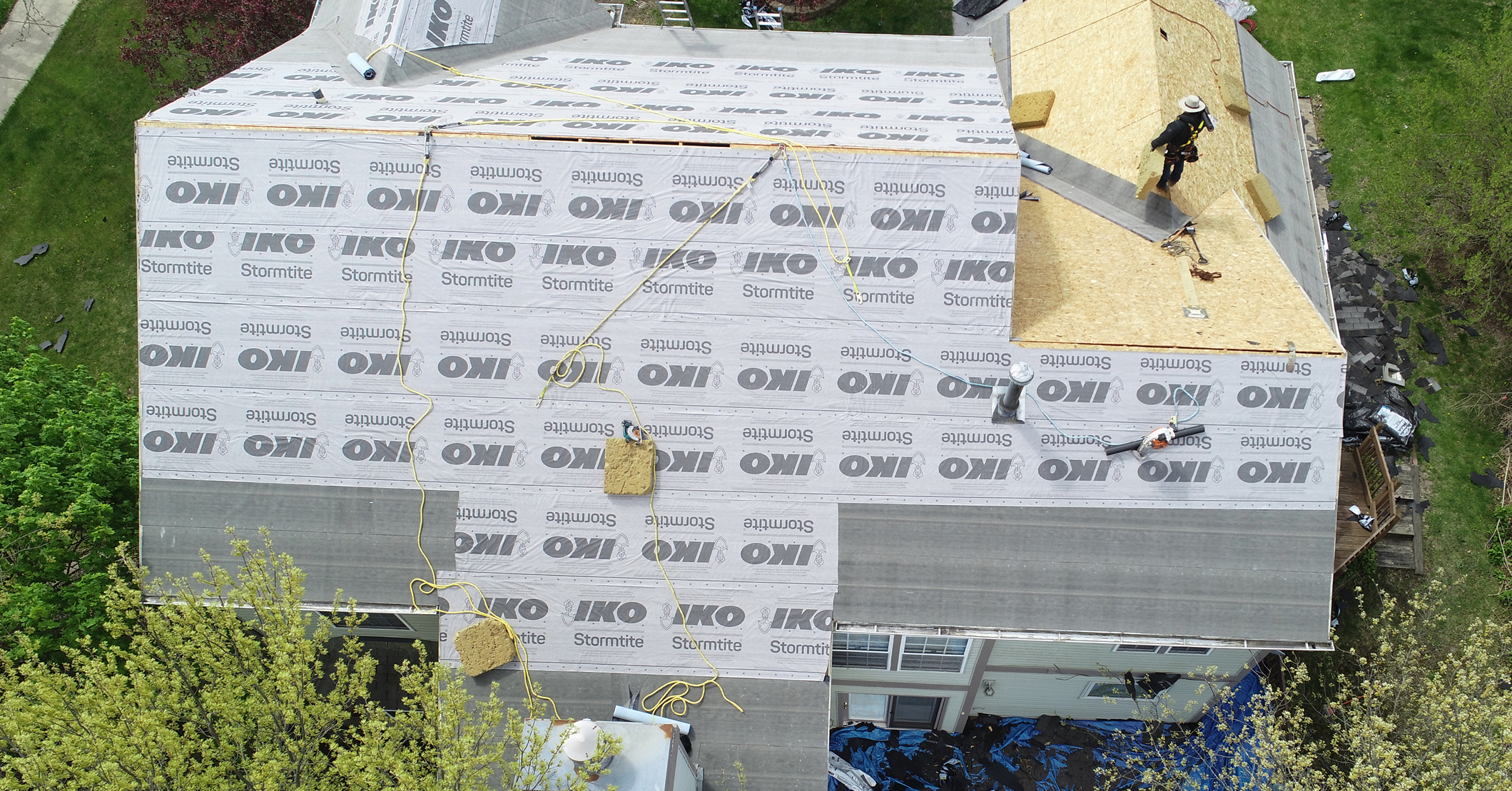 Bird’s-eye view of roof installation with multiple workers applying IKO Stormtite synthetic underlayment on a large house.