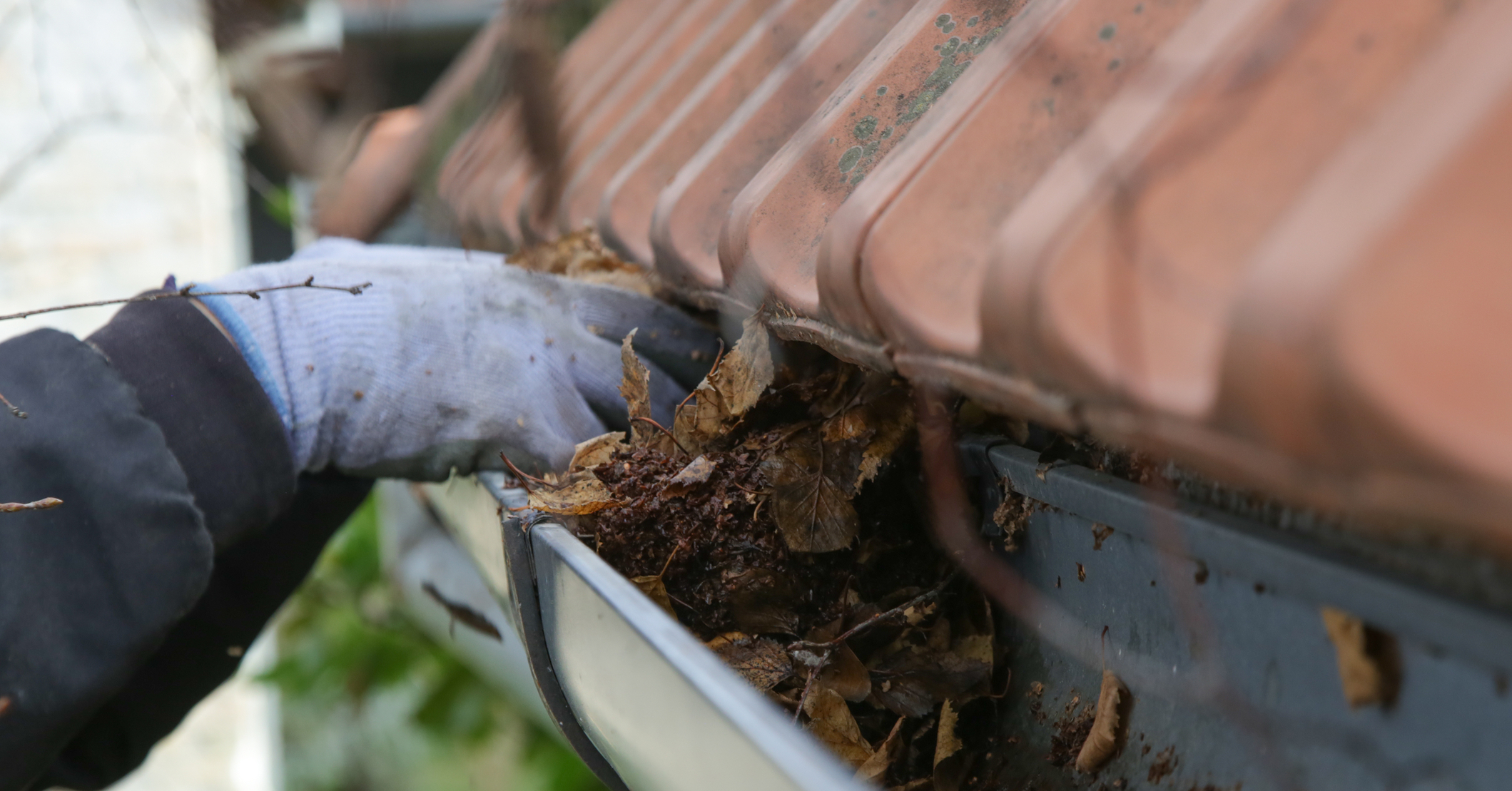 Hand clearing debris from clogged gutter during winter roof maintenance.