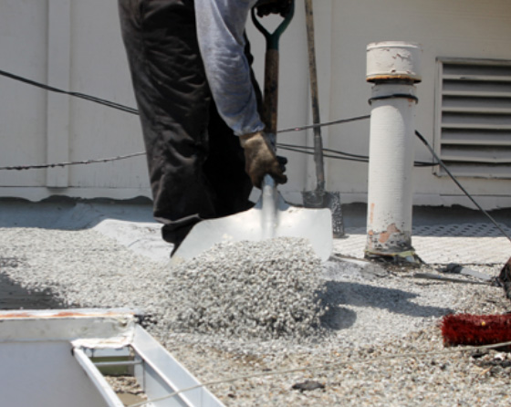 roofer shoveling gravel on top of a flat roof