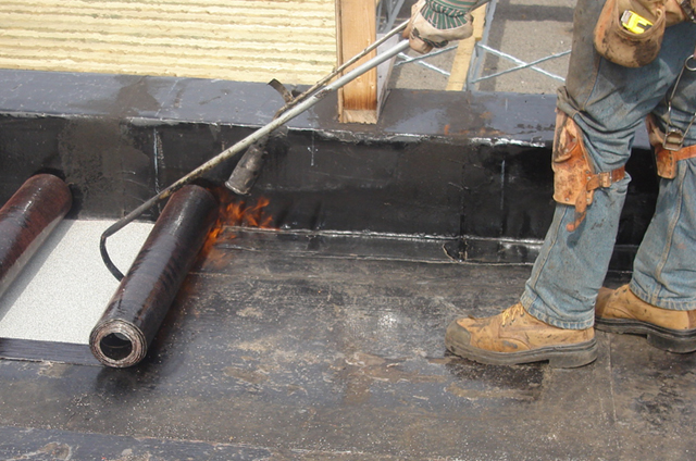 roofer using a gas torch to heat welding a roofing memrane