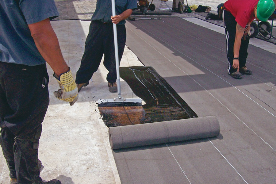 Roofers applying cold-applied Base Sheet membrane using a squeegee