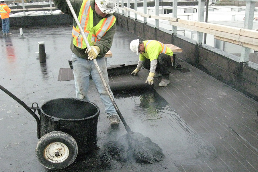 roofers applying felts on a BUR roof with a hot mop