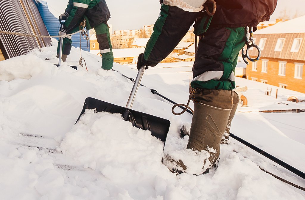 men using shovels to remove snow off commercial roof