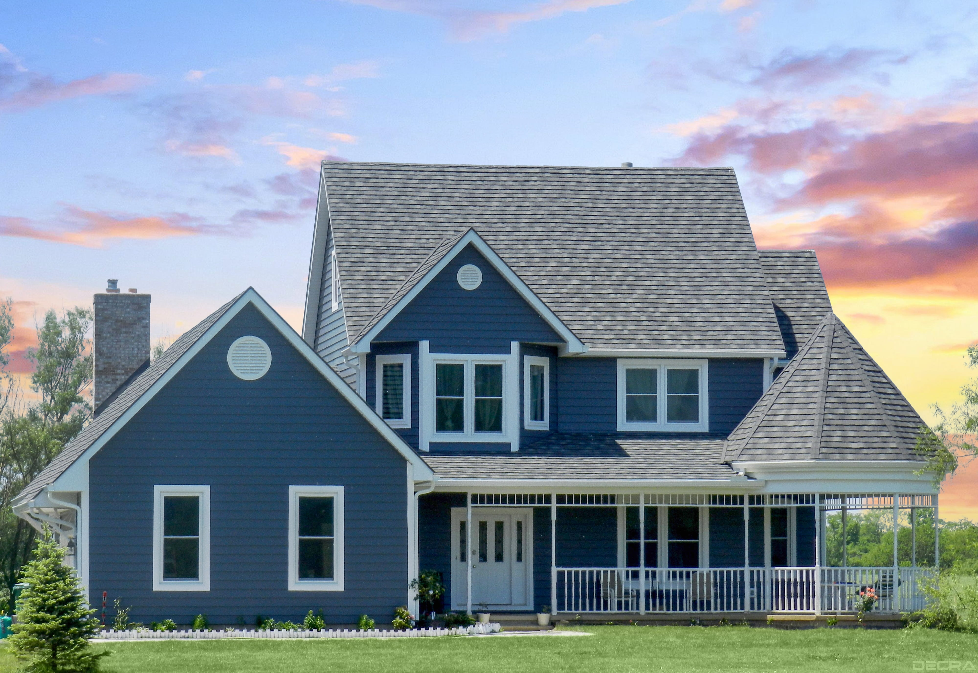 DECRA Shake gray metal roofing on a blue two-story farmhouse with wraparound porch at sunset, textured tile-look steel panels
