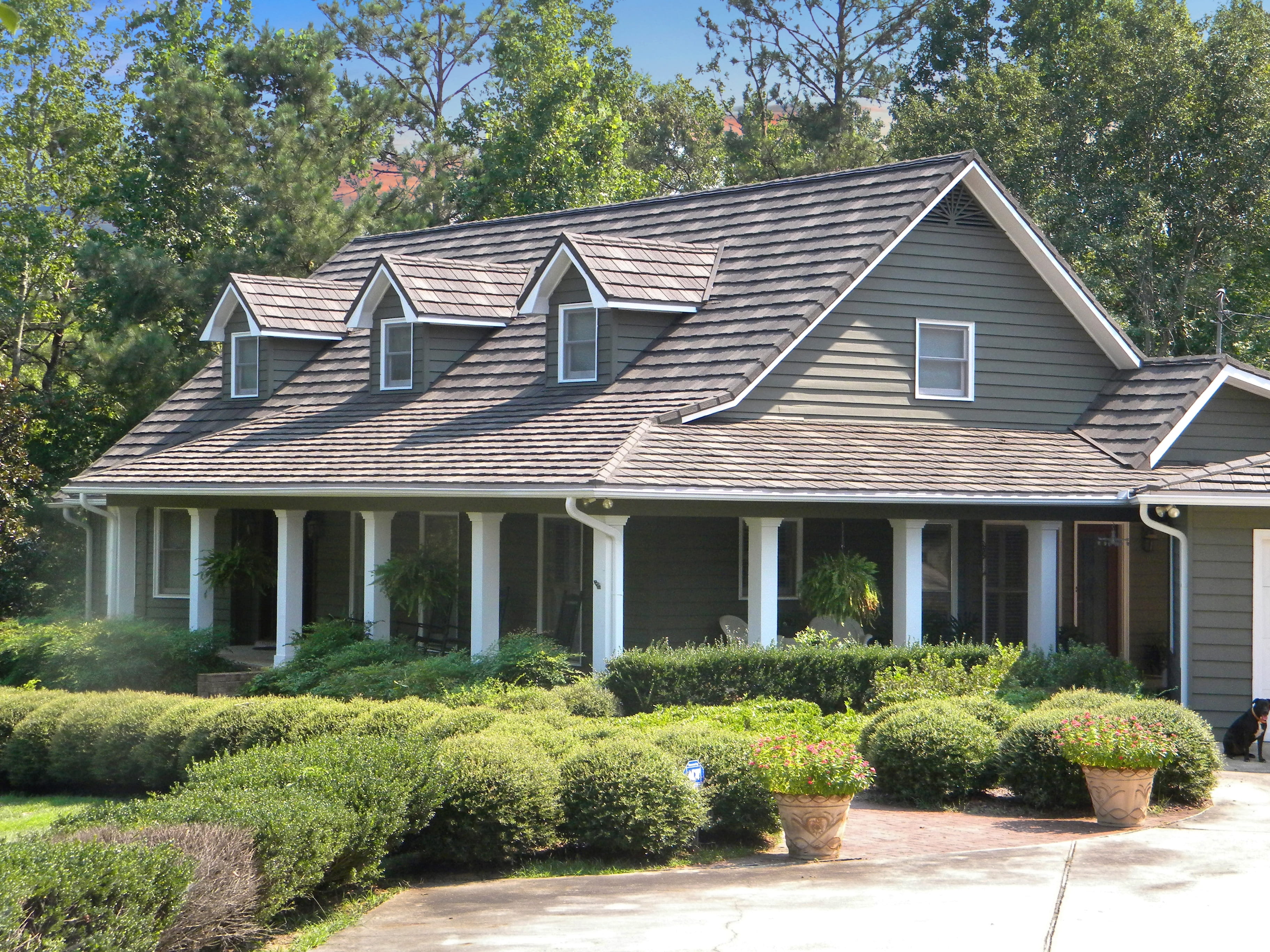 DECRA shake-profile metal roof on a gray Cape Cod-style home with a wraparound porch