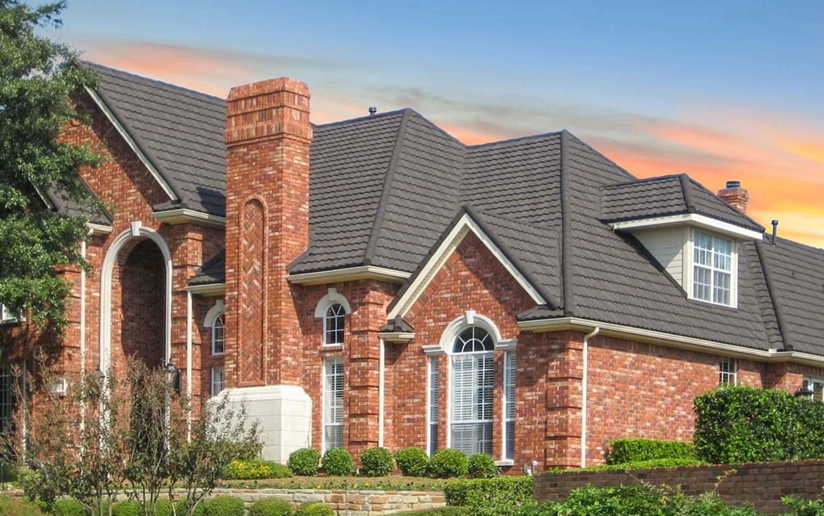 DECRA Mediterranean Scalloped Tile Carbon stone-coated steel roof on brick home, low-profile scalloped tiles at dusk