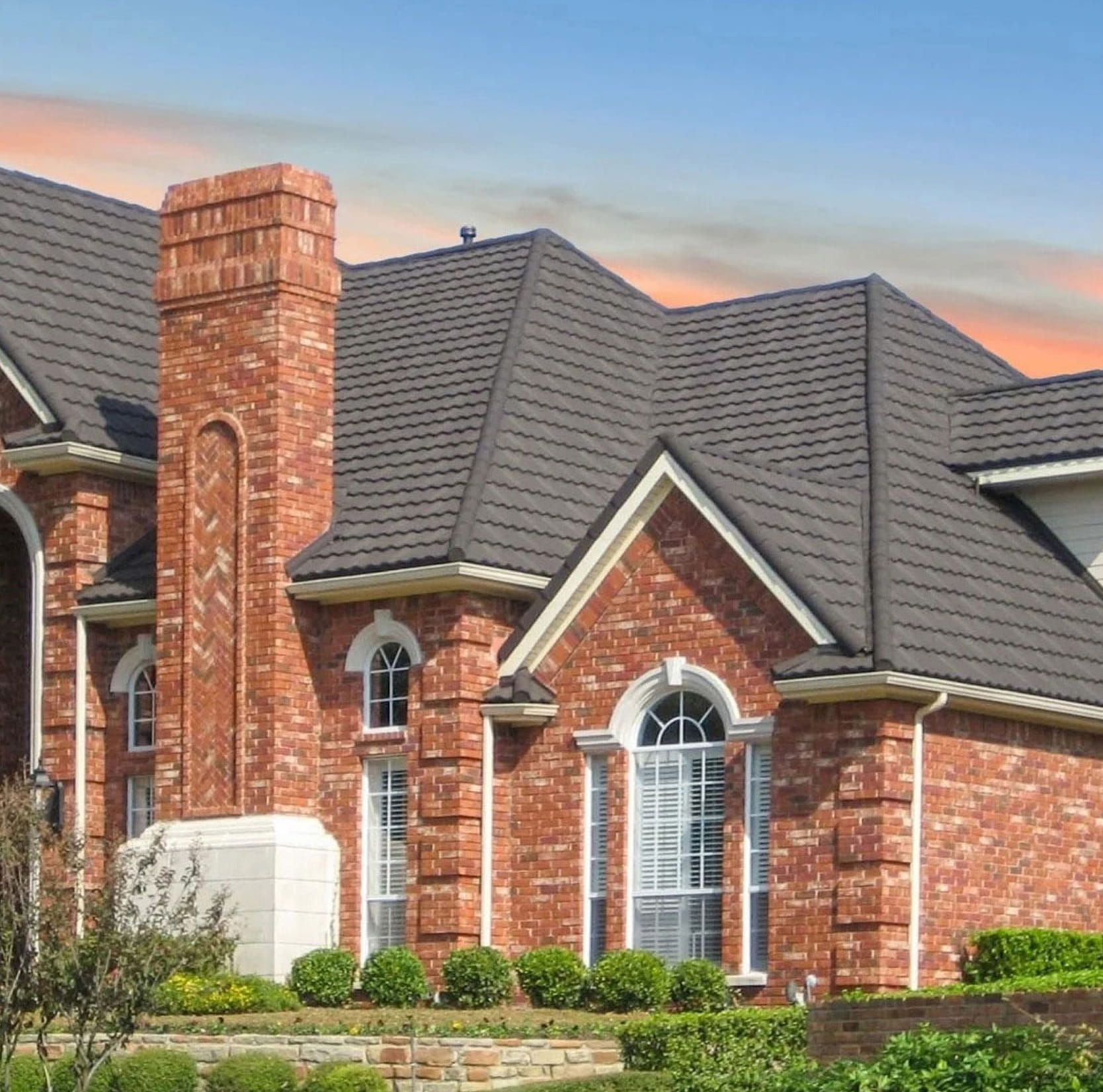 DECRA Mediterranean Scalloped Tile Carbon stone-coated steel roof on brick home, low-profile scalloped tiles at dusk