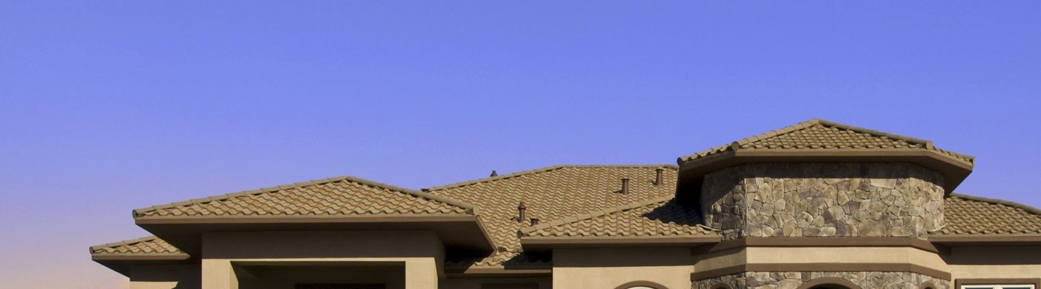 DECRA tan clay tile metal roofing on upscale stone-accented home beneath a clear blue sky, showing tile texture and profile