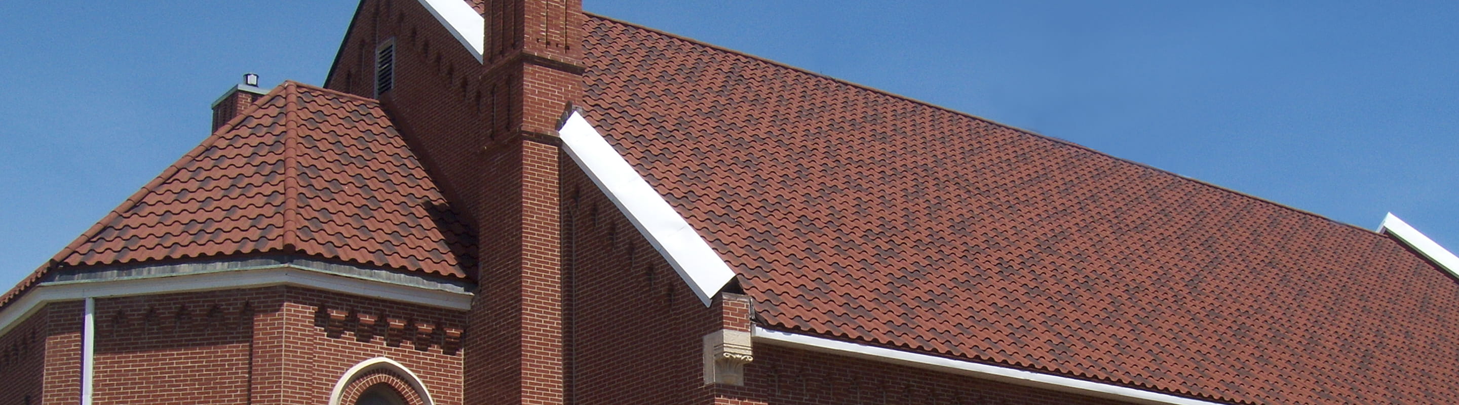 DECRA metal roofing on a red brick church with terra cotta stone-granule tile-look panels under a clear blue sky