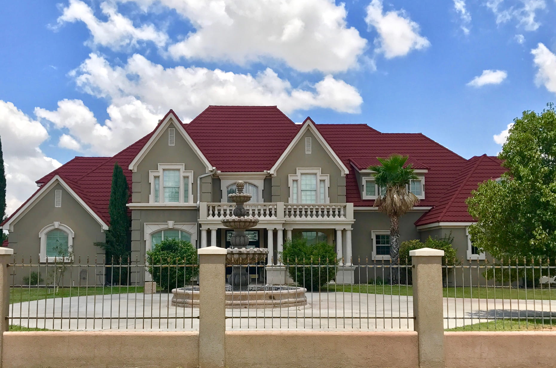 Deep red DECRA metal tile roof on elegant two-story home with fountain, columns and palm tree landscaping