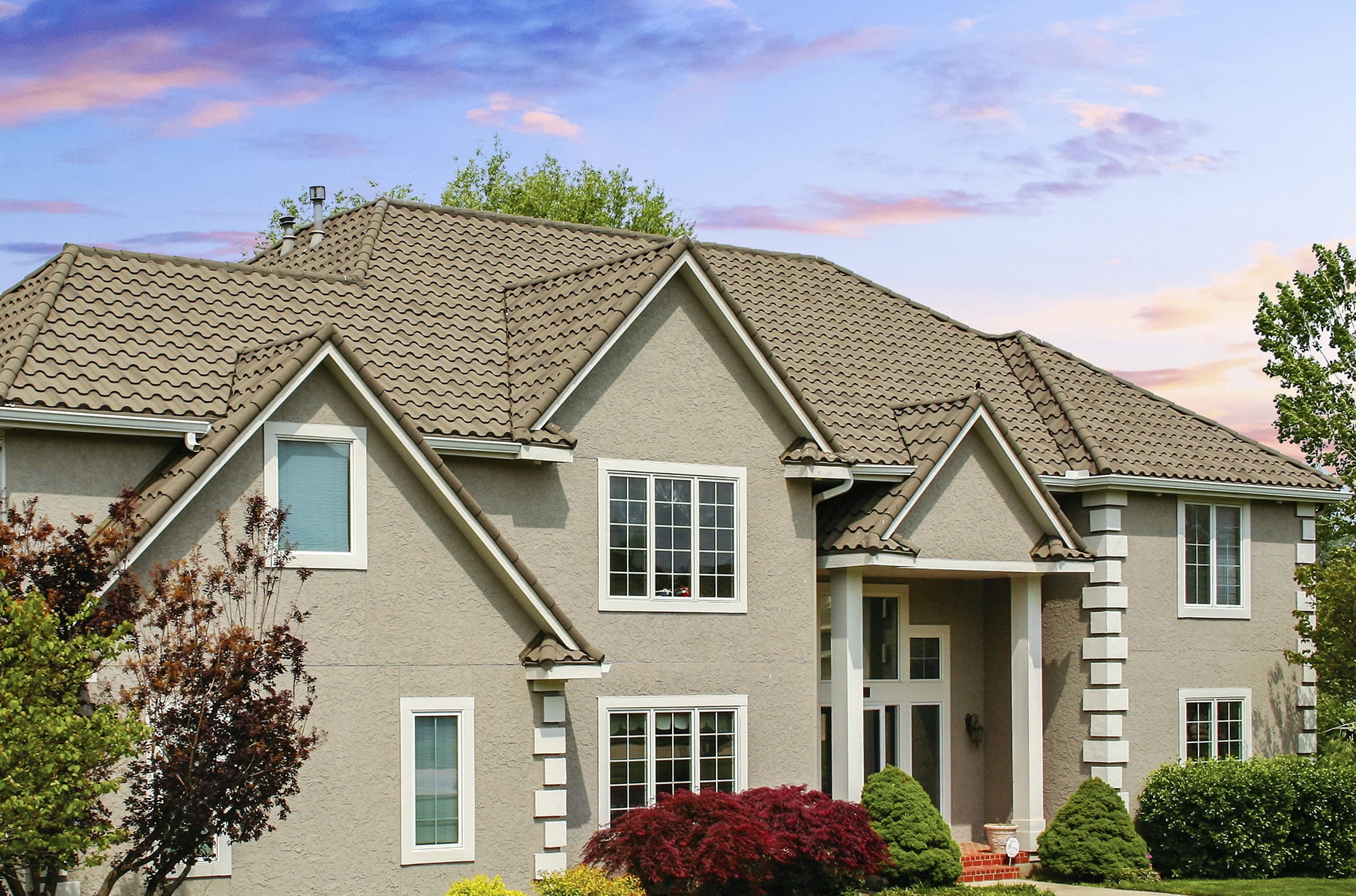 DECRA metal roof on upscale stucco home in tan stone-granule finish showcasing tile-look panels and classic gables at sunset