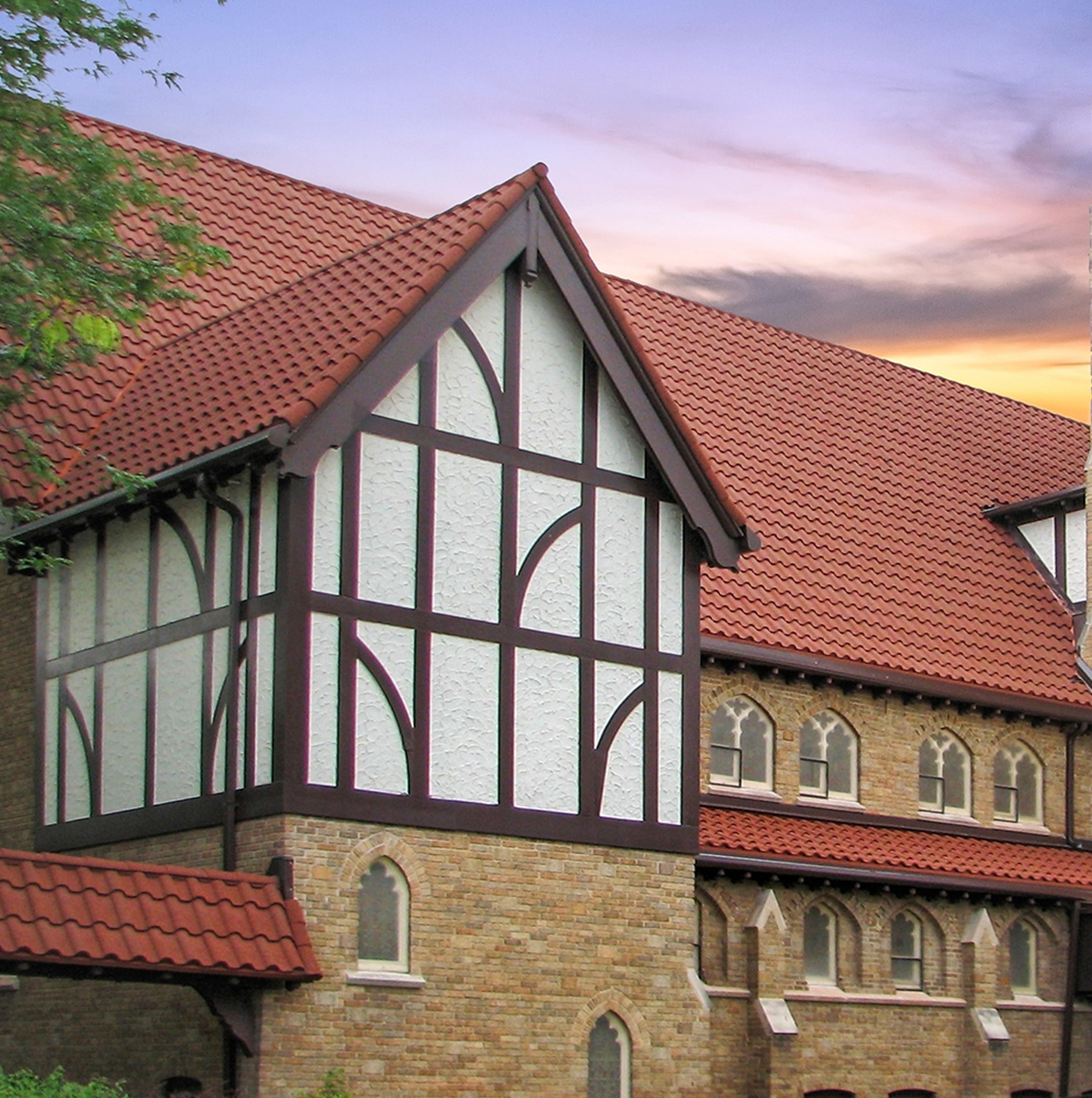 DECRA red tile metal roofing on Tudor-style church gable with white stucco and decorative timber framing at sunset