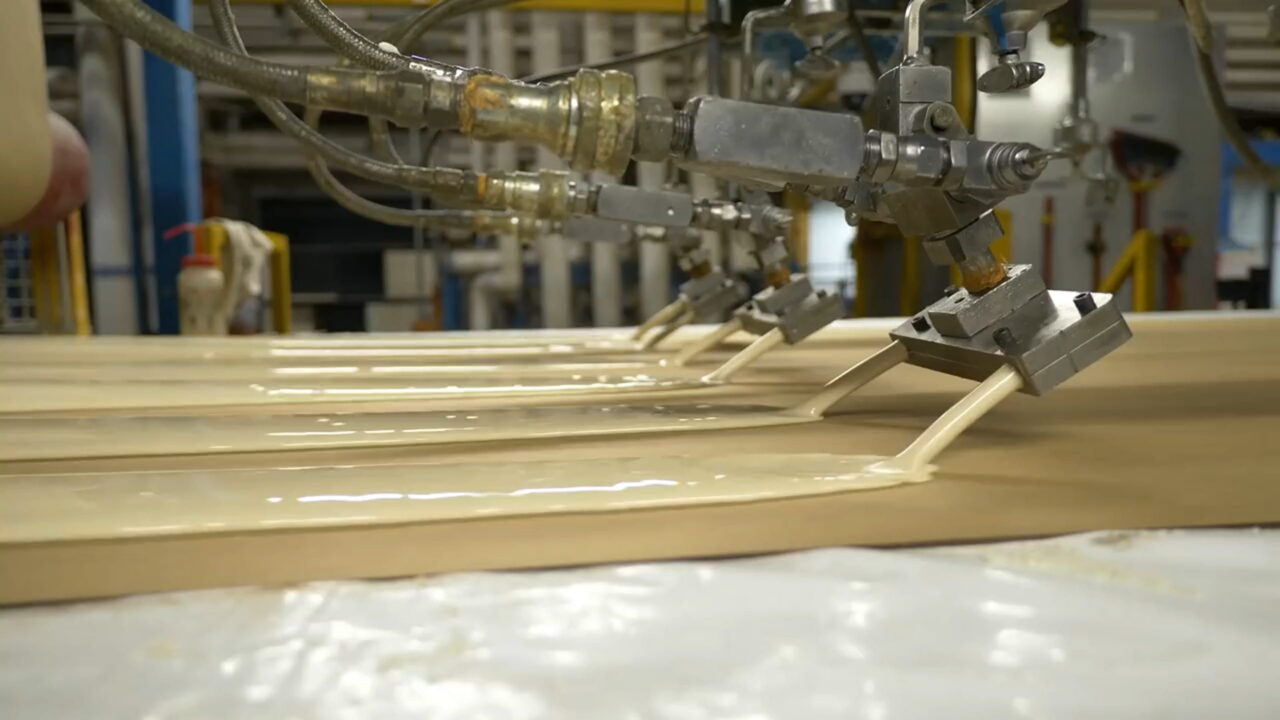 Industrial nozzles dispensing pale liquid foam onto a board on a production line at an IKO plant