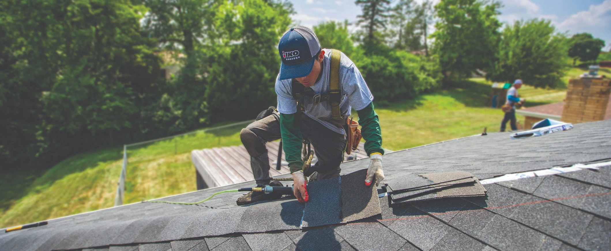 Roofer installing shingles while wearing an IKO hat.