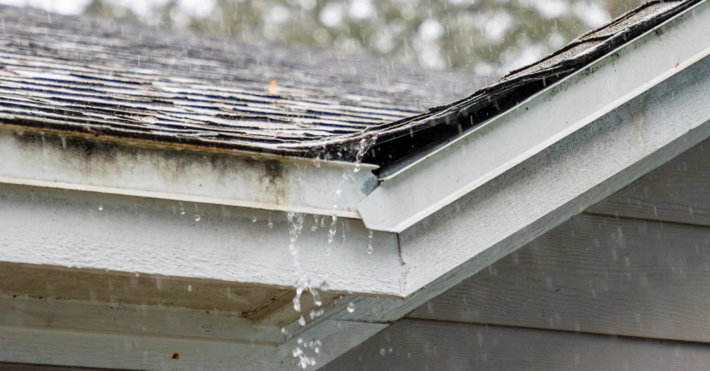 Worn, discolored shingles and flashing that are damaged. Heavy rain is pouring on them.
