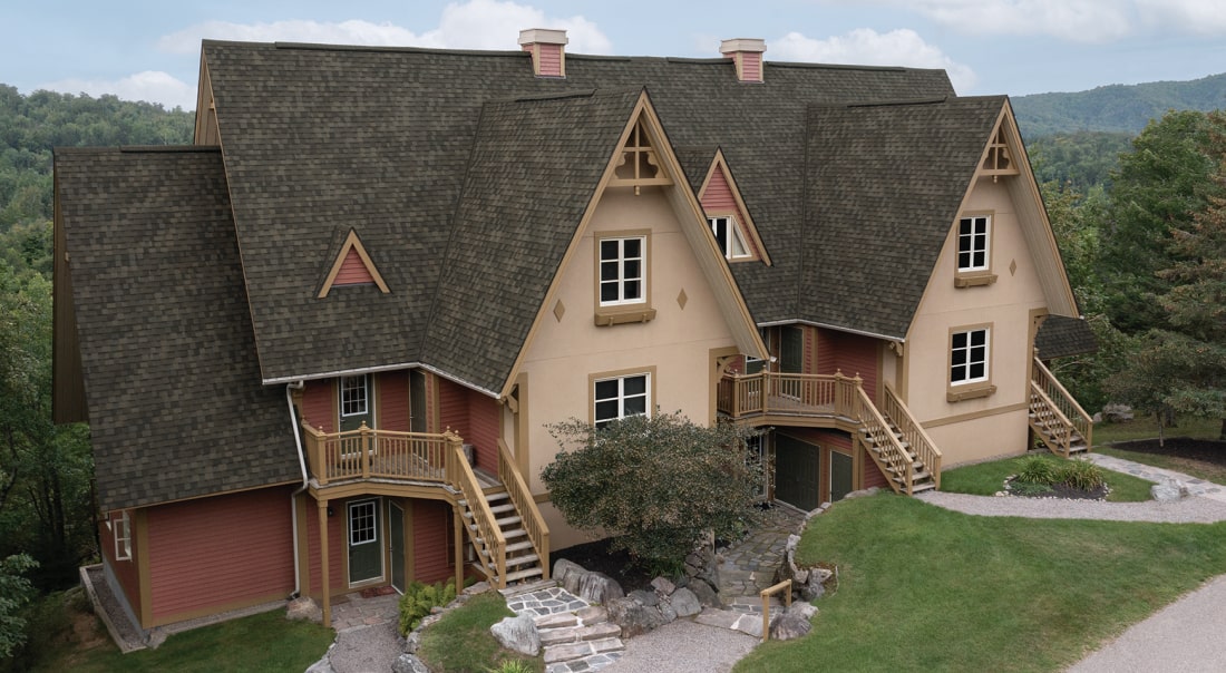 Un bâtiment de style chalet Nordic™ aux toits à pignon à forte pente, aux accents de bois et aux escaliers extérieurs est joliment entouré de verdure luxuriante.