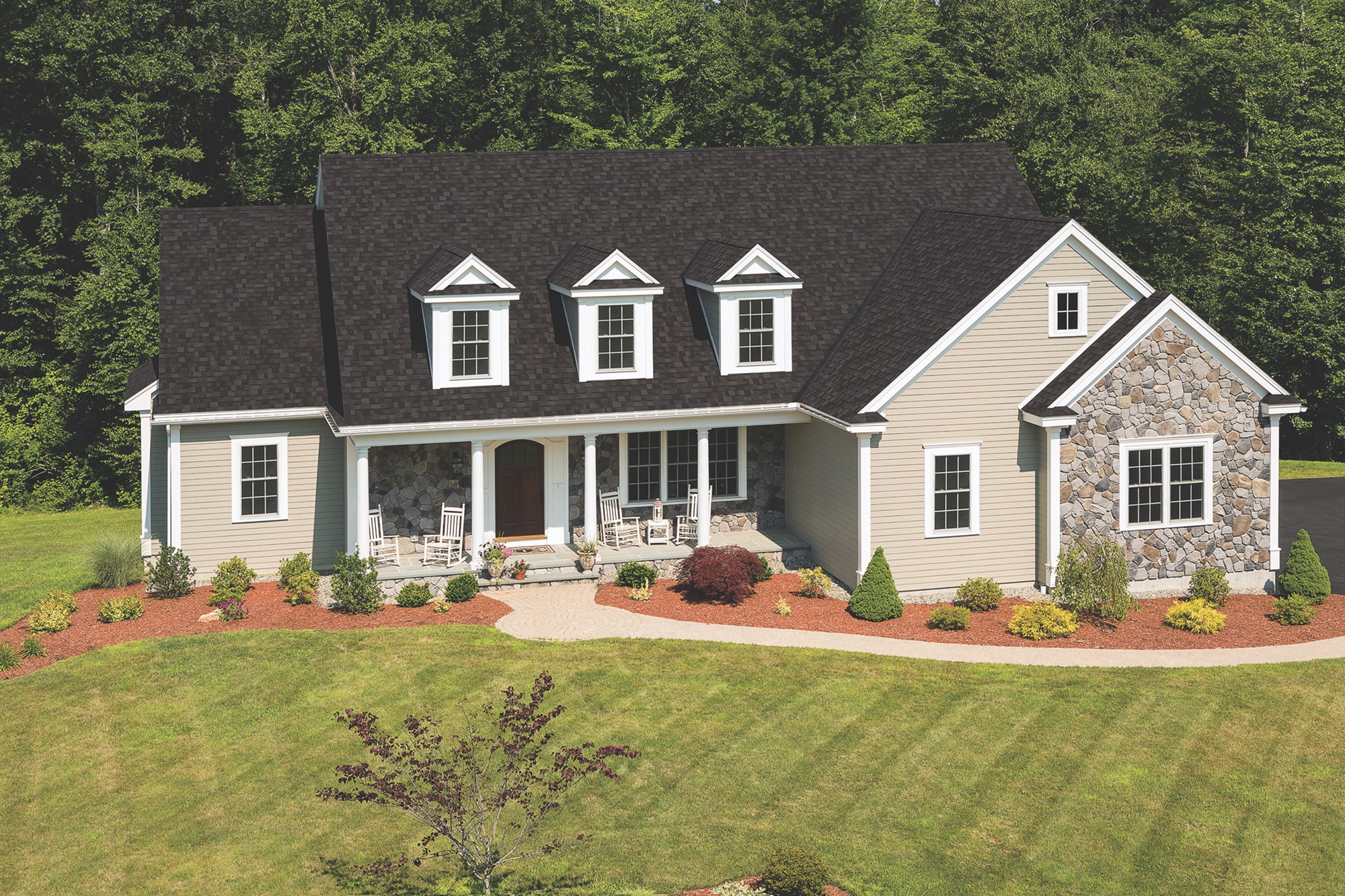 Aerial view of a home with three dormers, a dark Cambridge shingle roof and a landscaped lawn