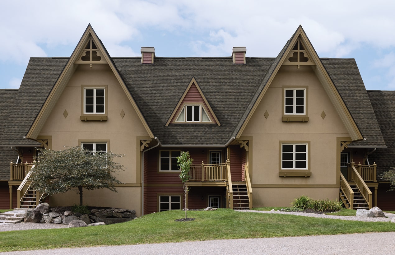Un bâtiment de style chalet Nordic™ aux toits à pignon à forte pente, aux accents de bois et aux escaliers extérieurs est joliment entouré de verdure luxuriante.