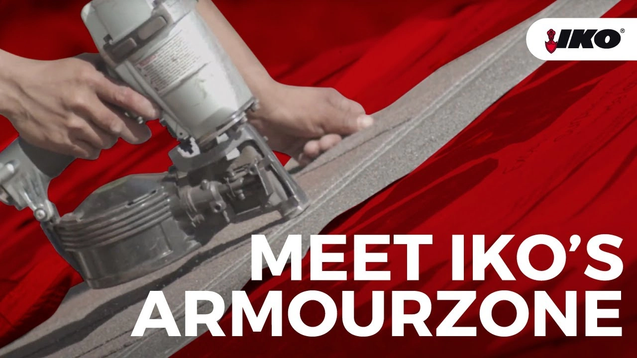 Close-up of hands expertly using a tool on roofing material. The red backdrop boldly features the text "Meet IKO's Reinforced Nailing Zone" alongside the iconic IKO logo.