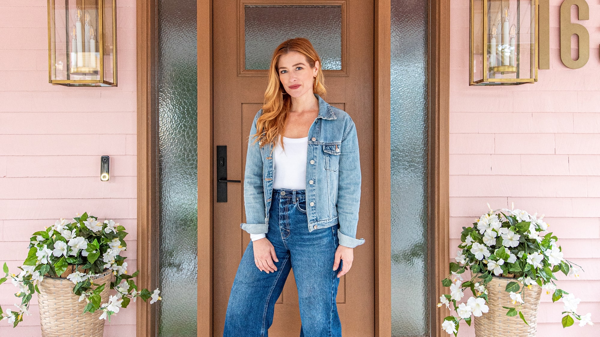 Rebekah Higgs in a denim jacket standing in front of a wooden door and pink siding