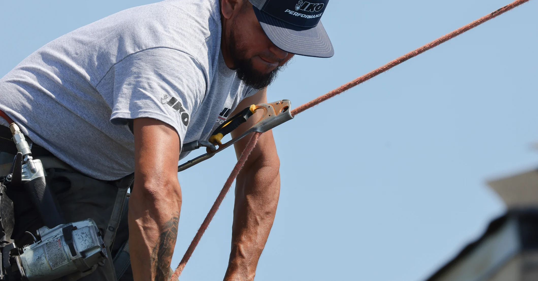 A close-up of a roofer wearing a safety harness and rope system.
