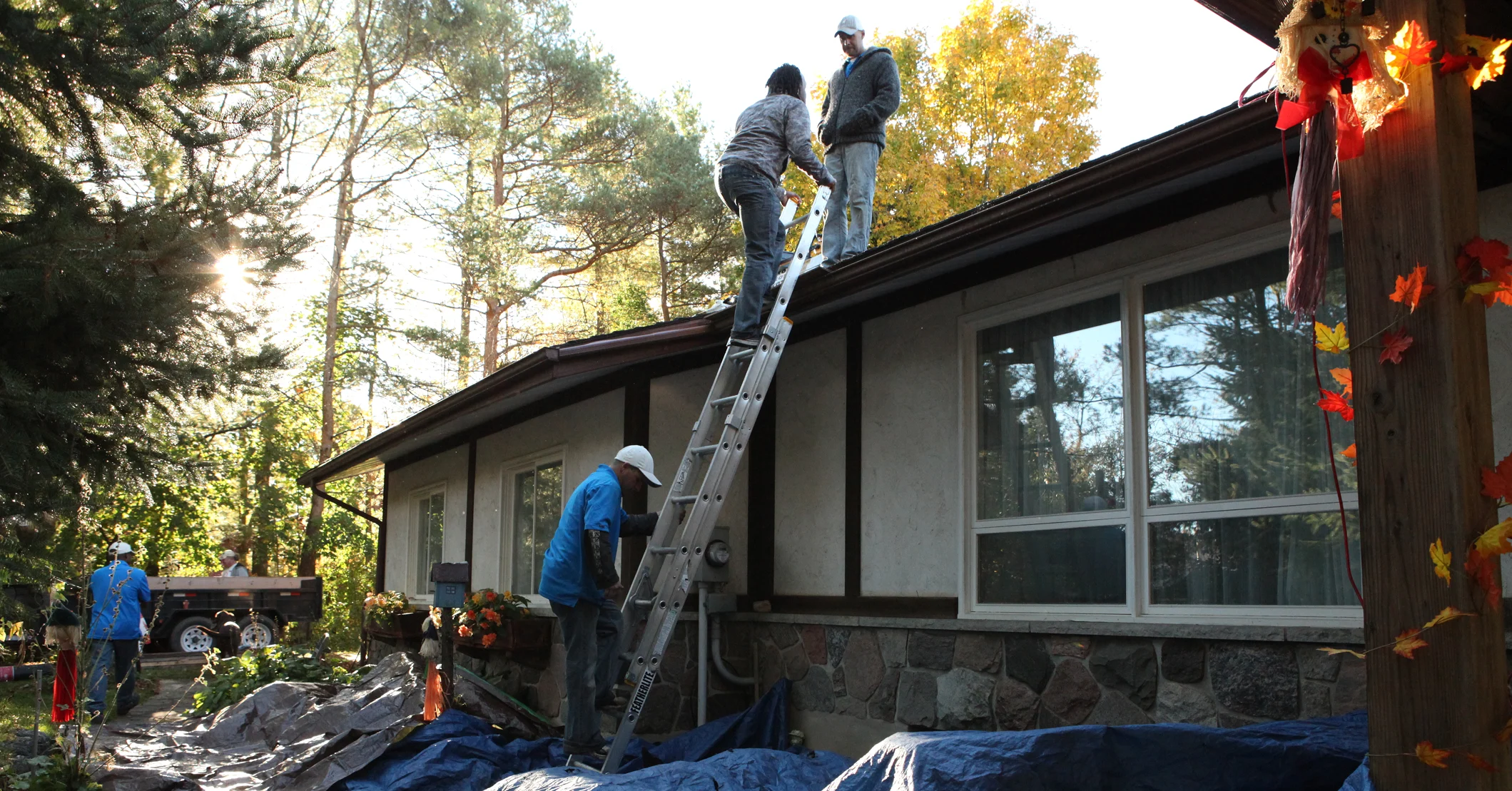A team of roofers using an extension ladder to work on a residential roof.