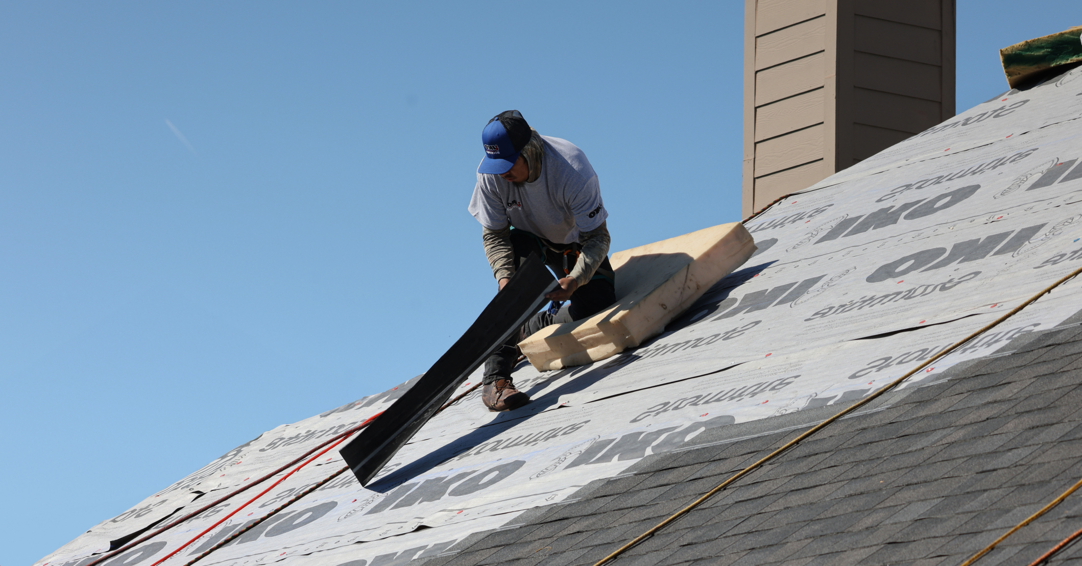Roofing contractor installing a water-resistant barrier on a residential roof before shingle installation. The worker is securing roofing underlayment to prepare for new shingles.