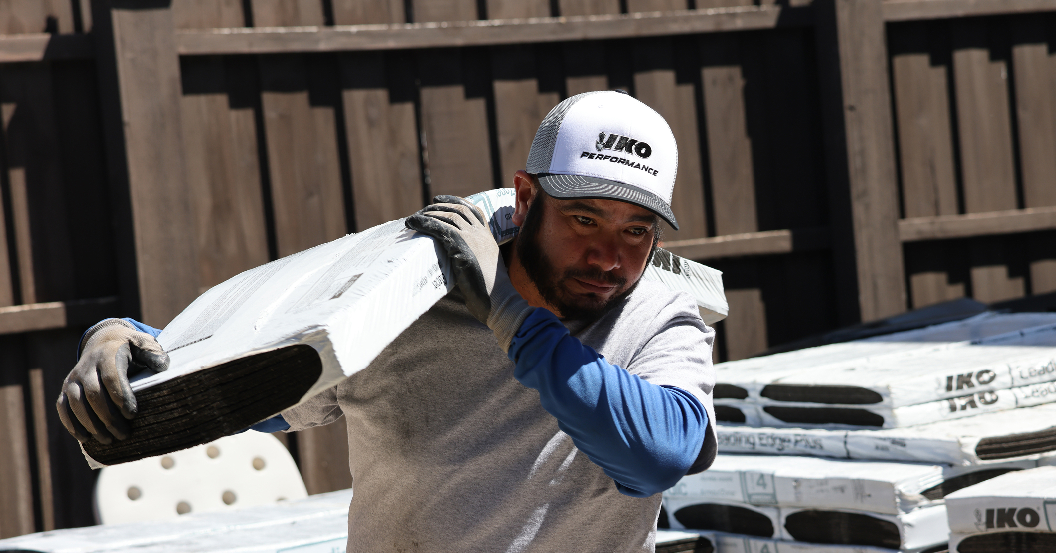 Worker carrying a bundle of shingles on his shoulder at a roofing job site.
