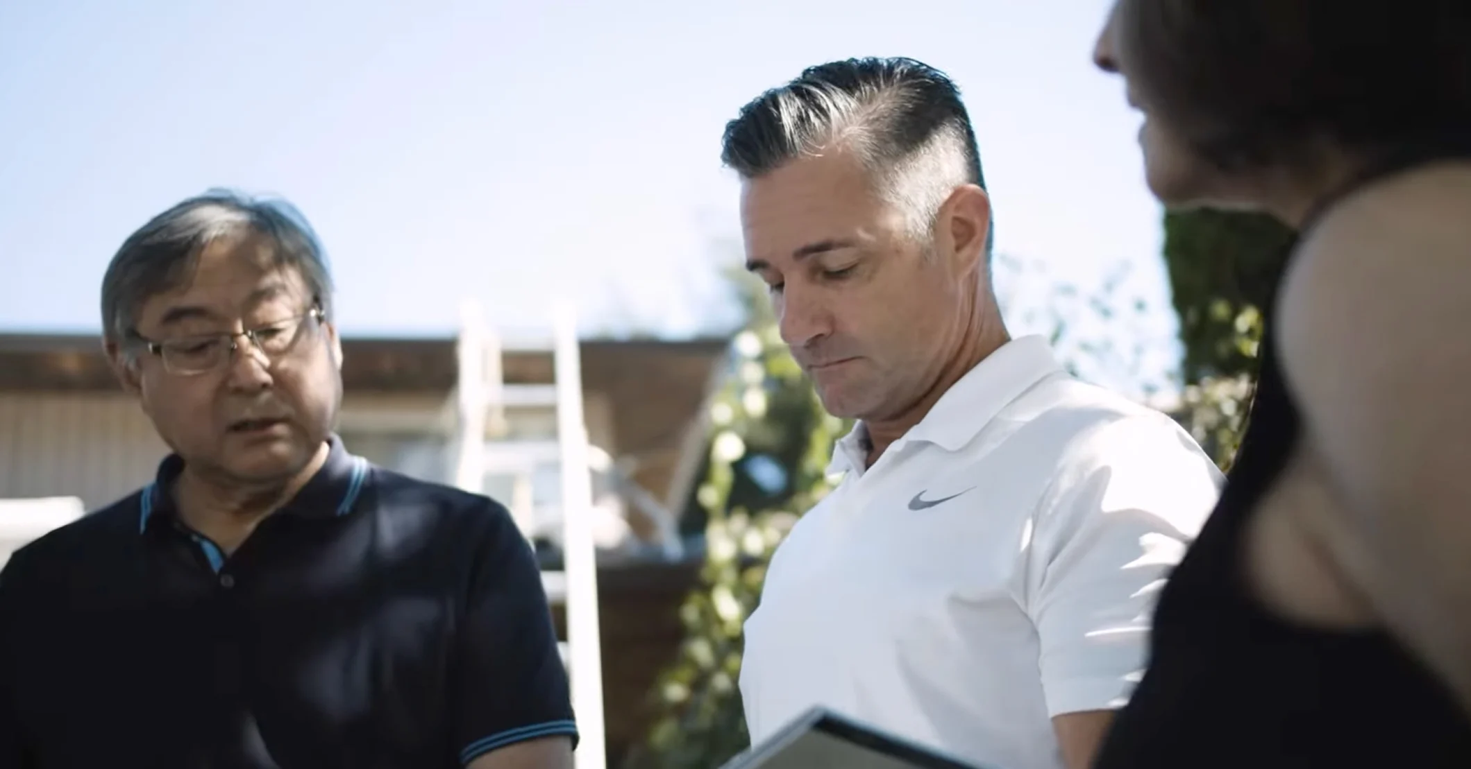 A roofing contractor reviews project details outdoors with two homeowners.