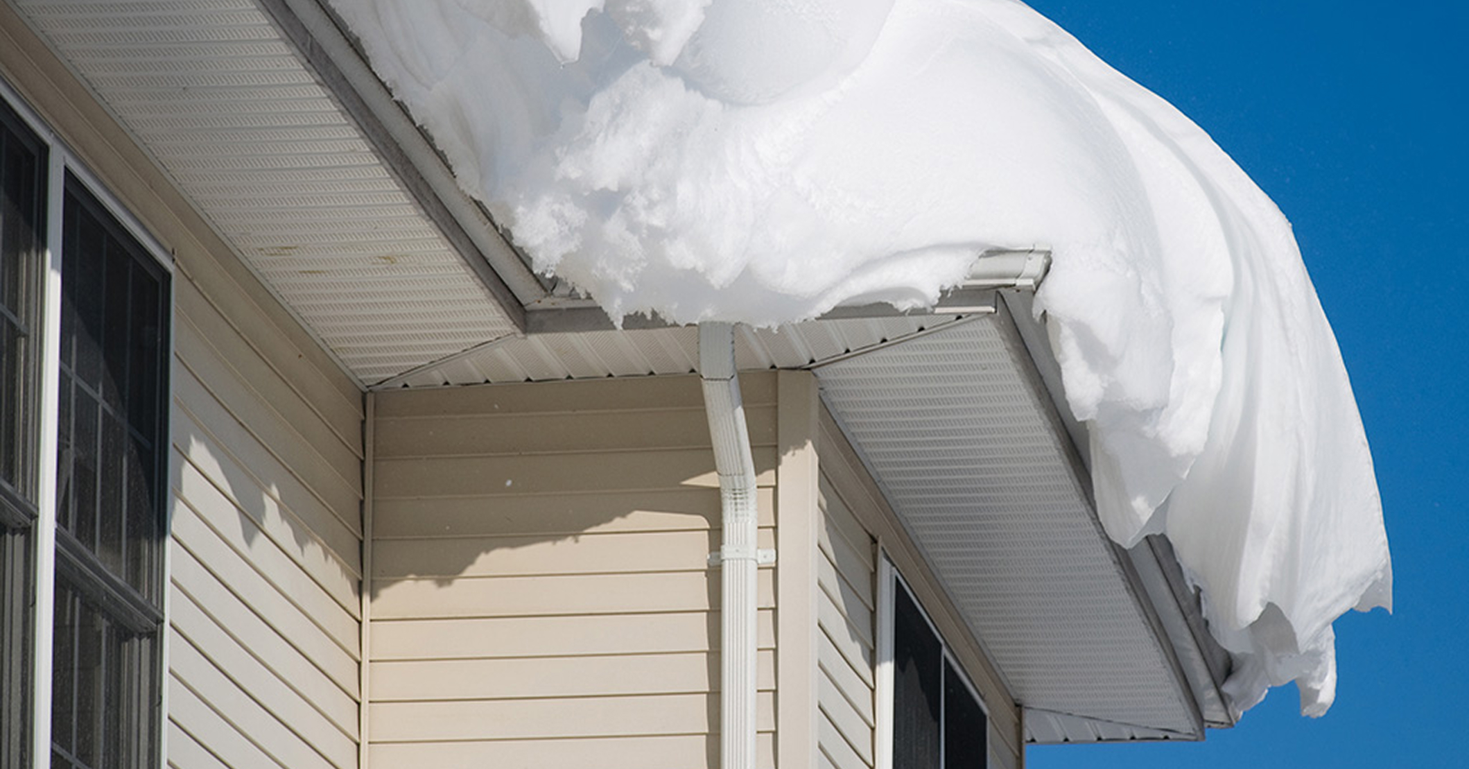 Heavy snow buildup on a light-colored home’s roof and gutters, highlighting winter weather impact on roofing