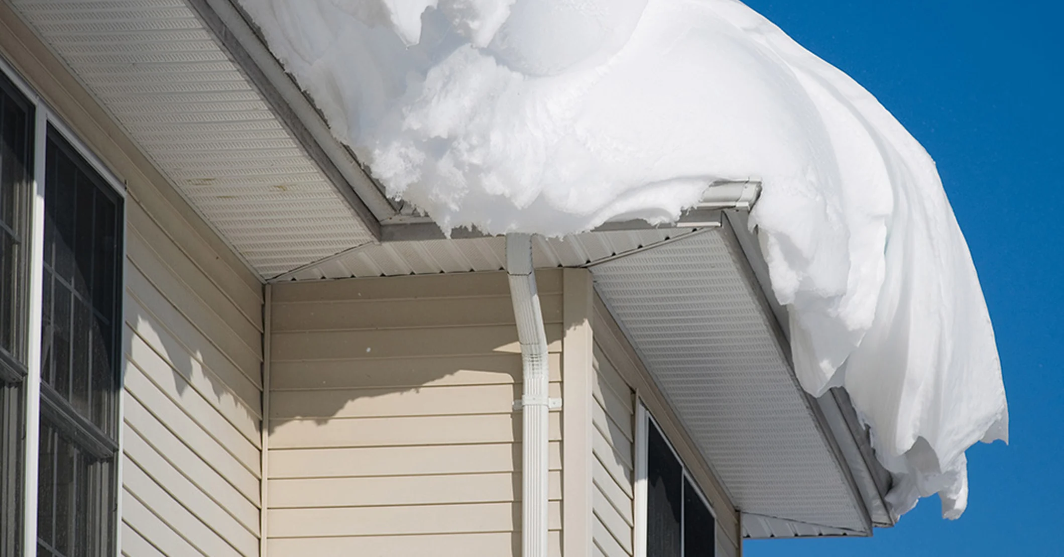 Heavy snow buildup on a light-colored home’s roof and gutters, highlighting winter weather impact on roofing