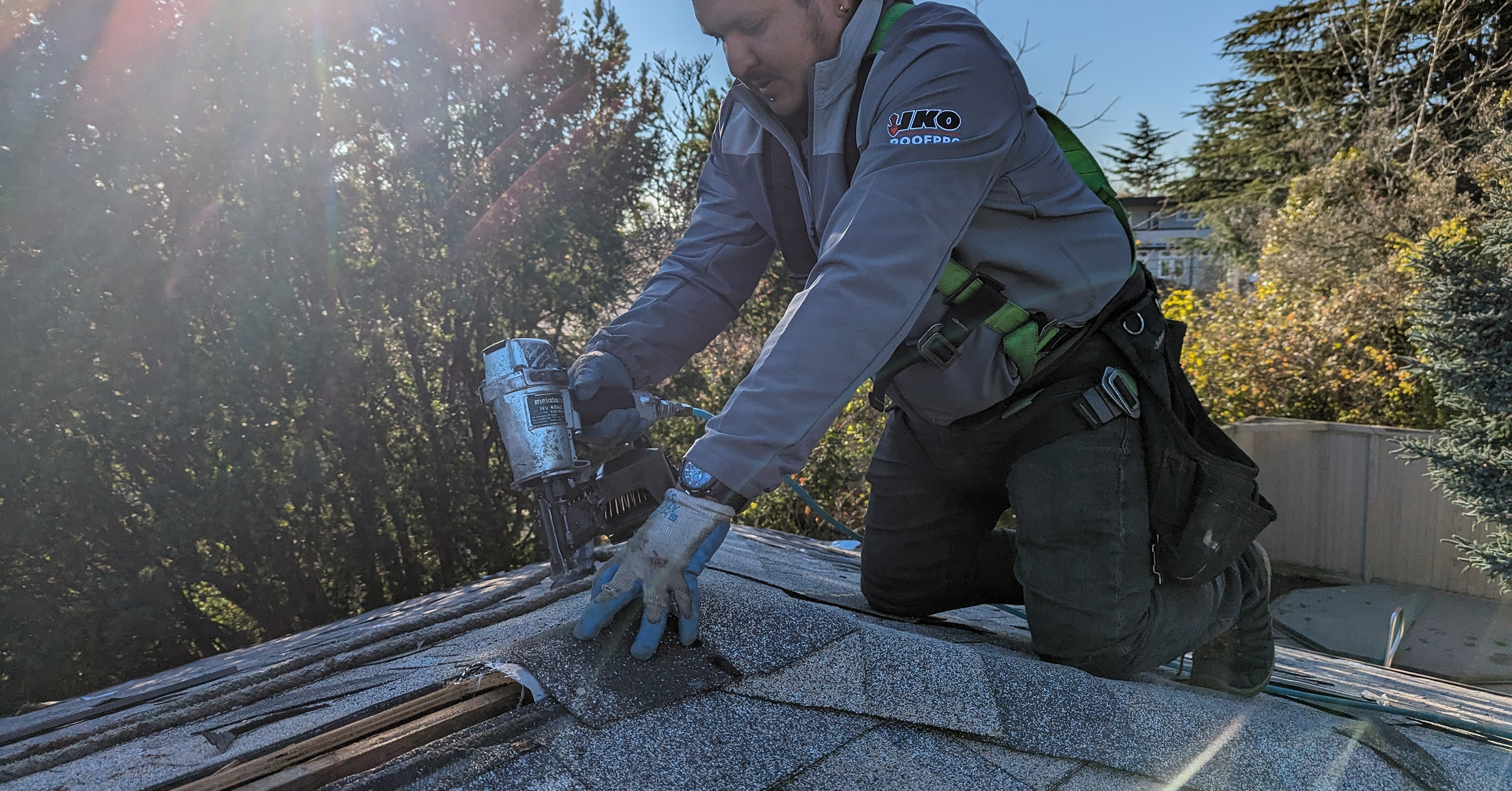 Licensed roofer using nail gun to replace missing shingles on residential roof.
