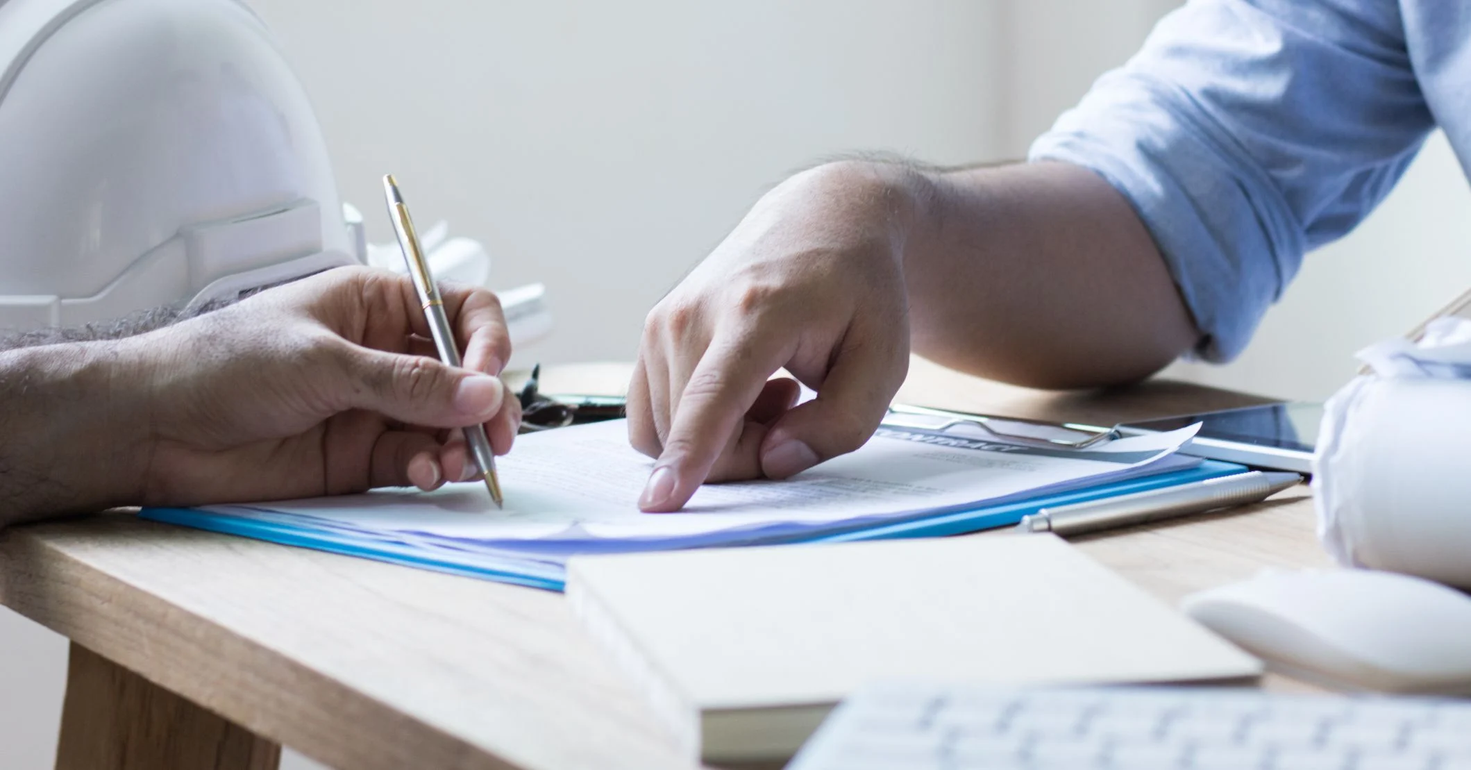 A contractor with a hard hat signs loan documents as a banker points to the signature line.