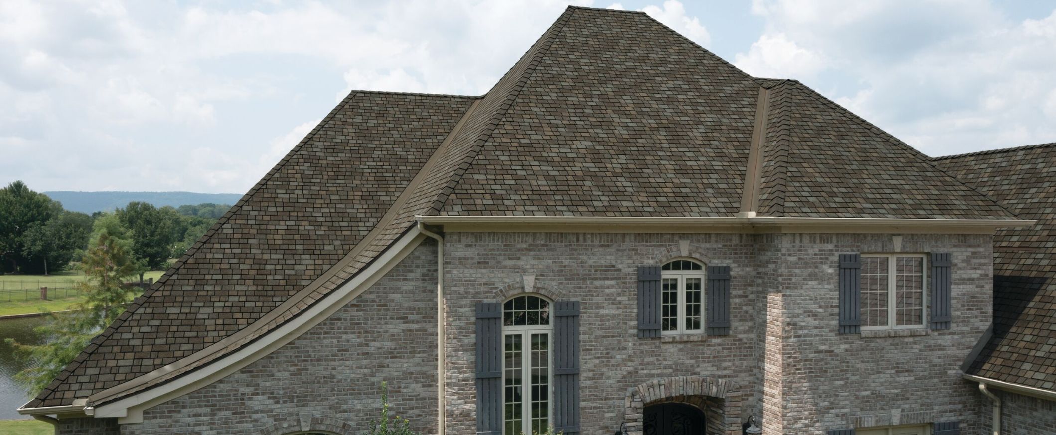 Large stone house with a steep, gently curved dark shingle roof overlooking a green valley