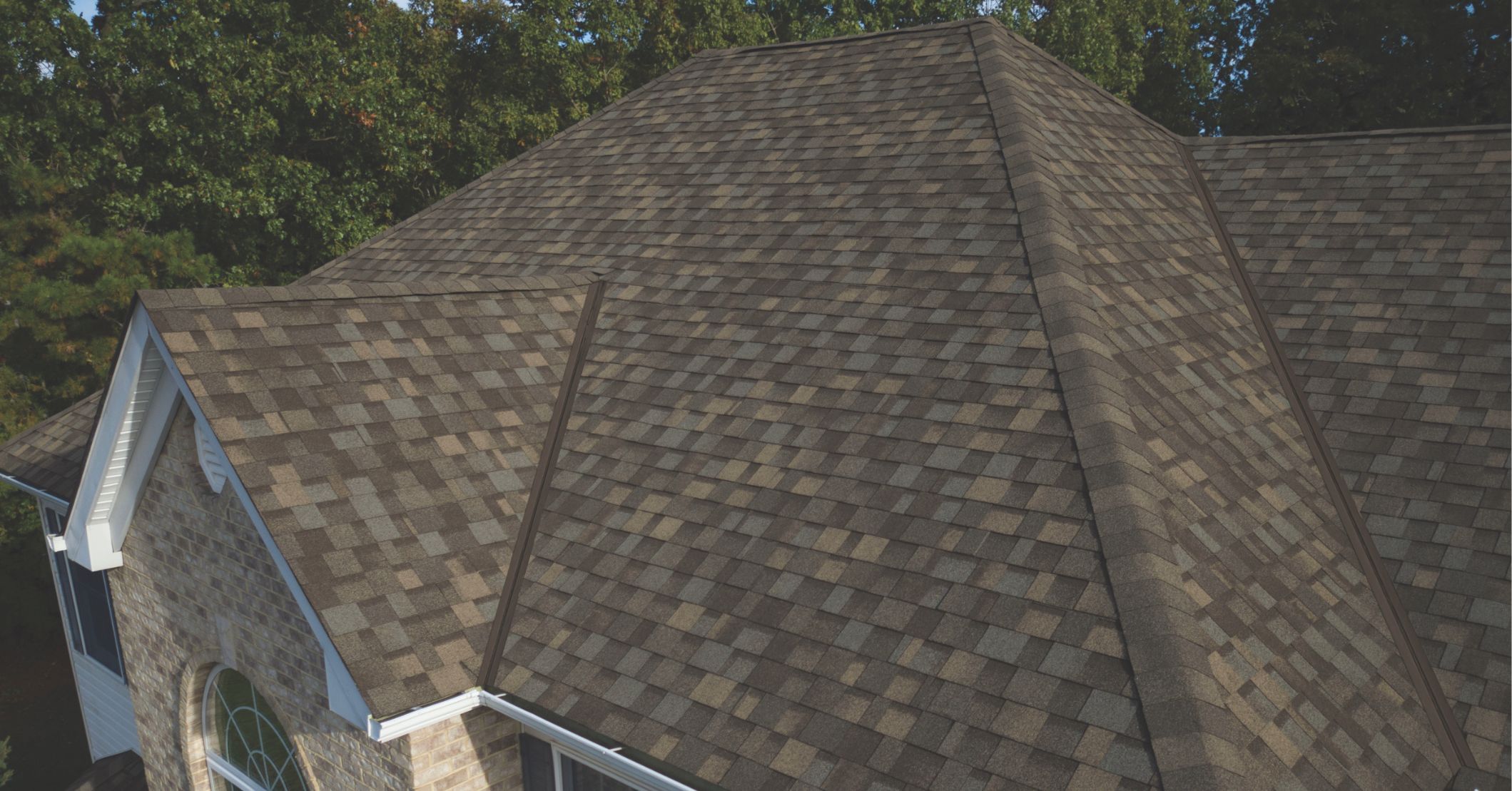 A high-angle, close-up view of a roof with textured, multi-toned brown and grey asphalt shingles.
