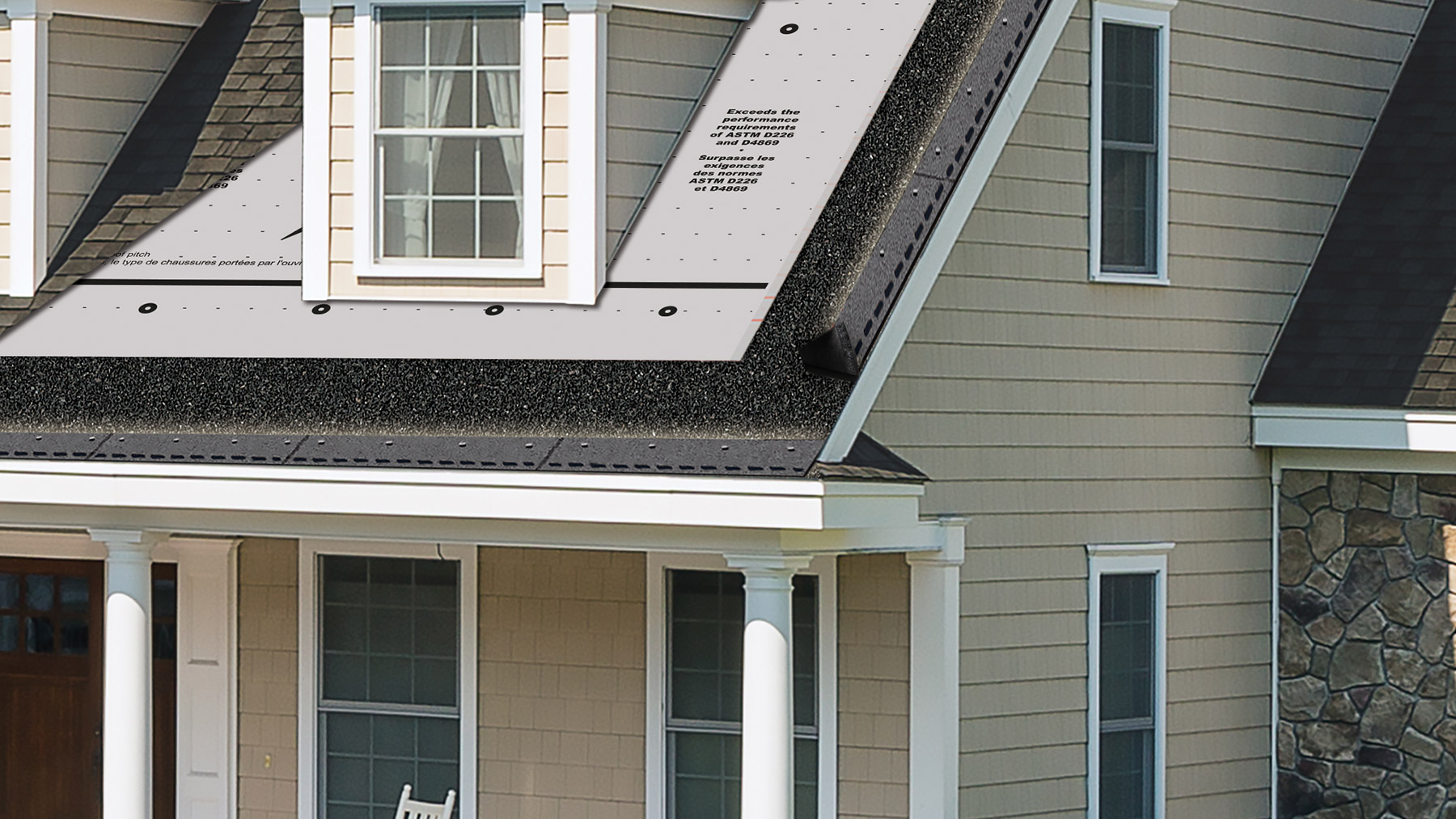 Beige-sided house with a dormer and a roof section covered in gray synthetic underlayment above dark shingles