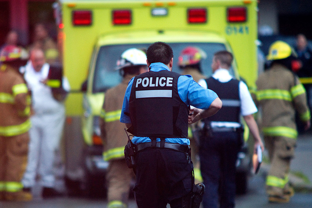 Police officer, firefighters and paramedics gathered around a yellow ambulance
