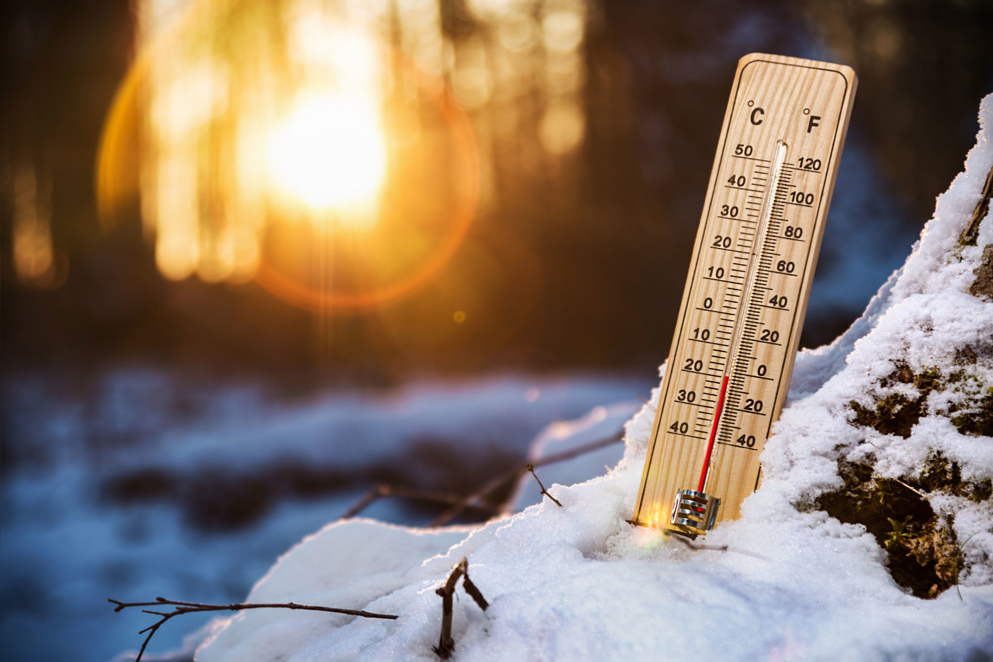 Wooden thermometer standing in snow with the sun low in the background showing a below-freezing temperature