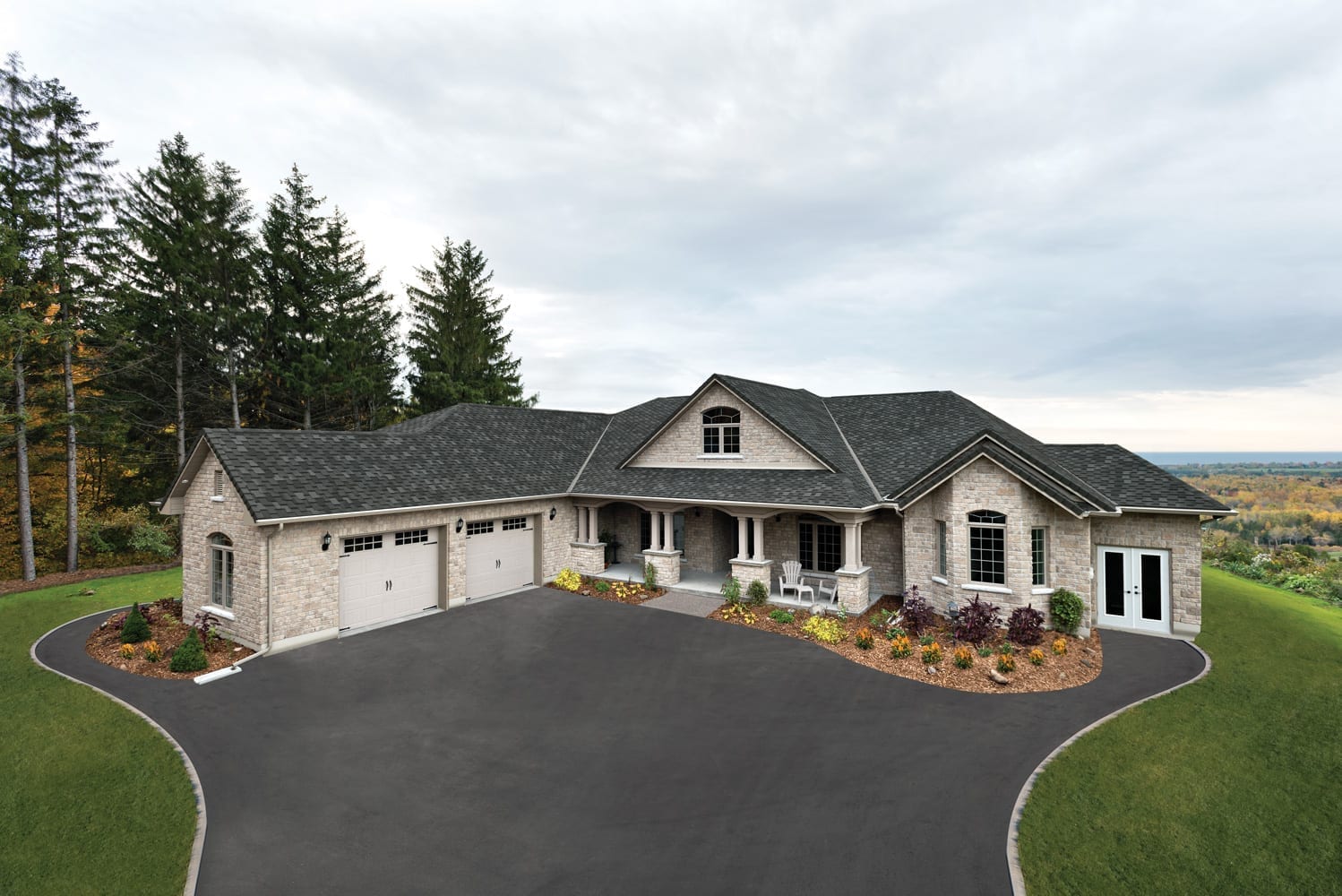 Single-story stone house with an IKO Armourshake Shadow Black shingle roof and a long paved driveway