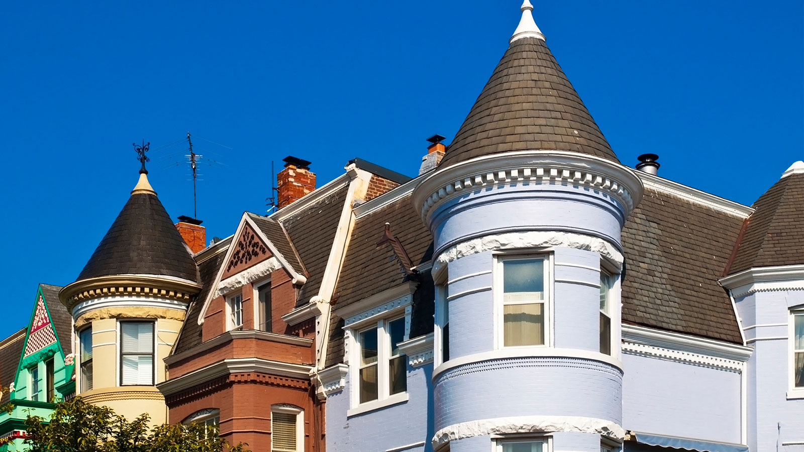 Colorful Victorian-style houses with conical turret roofs and dark shingles against a deep blue sky