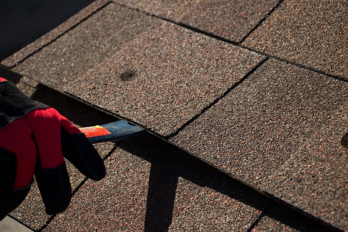 close view of a pry bar being used to lift a damaged shingle