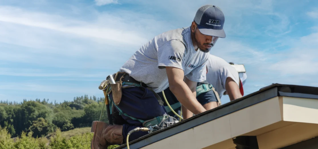 Roofing contractor installing shingles on a residential roof, using professional tools and safety gear.